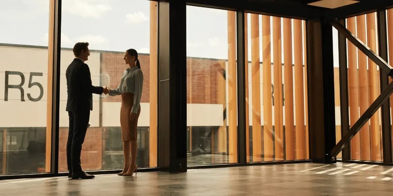 Two business people shaking hands in an office with timber-slatted windows